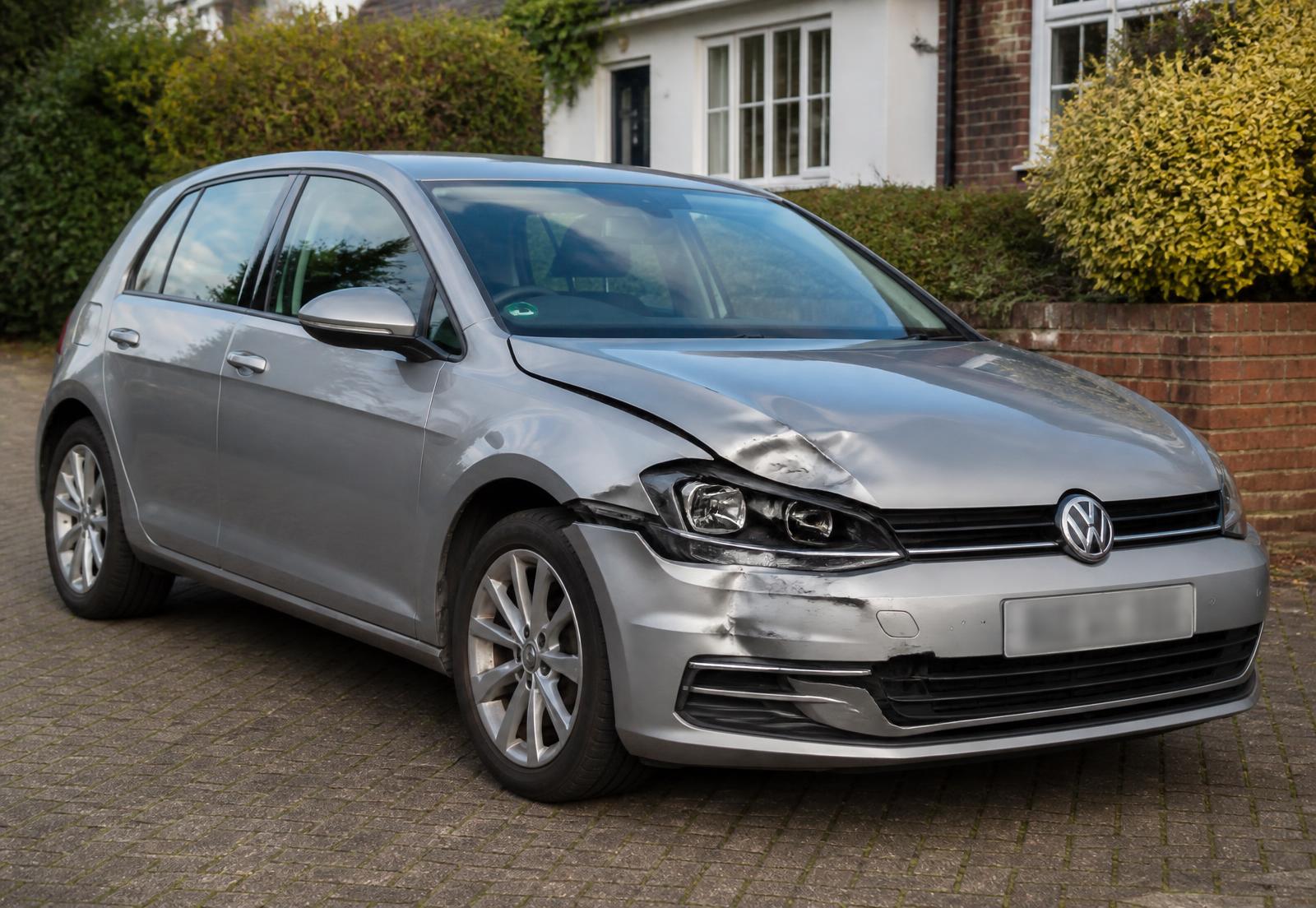 Silver family hatchback with front-corner accident damage awaiting assessment on a UK driveway